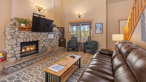 A cozy living room with a stone fireplace, leather sofa, and a flat-screen TV mounted above it.