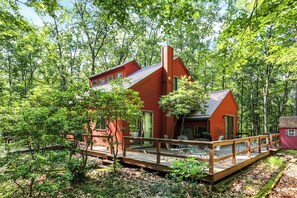 A red cabin with a wooden deck and outdoor seating area surrounded by dense forest. - Raystown Retreat- Snyders Run, Aunt Susie's (Huntingdon)
