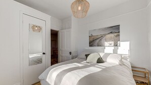 A bedroom with a large bed, a wooden floor, a white door, and a hanging light fixture. - Le Patrimonial-Two bedrooms 6 persons (Québec City)