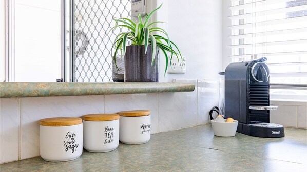 A kitchen with a coffee maker, three jars with motivational phrases, and a potted plant on the counter.