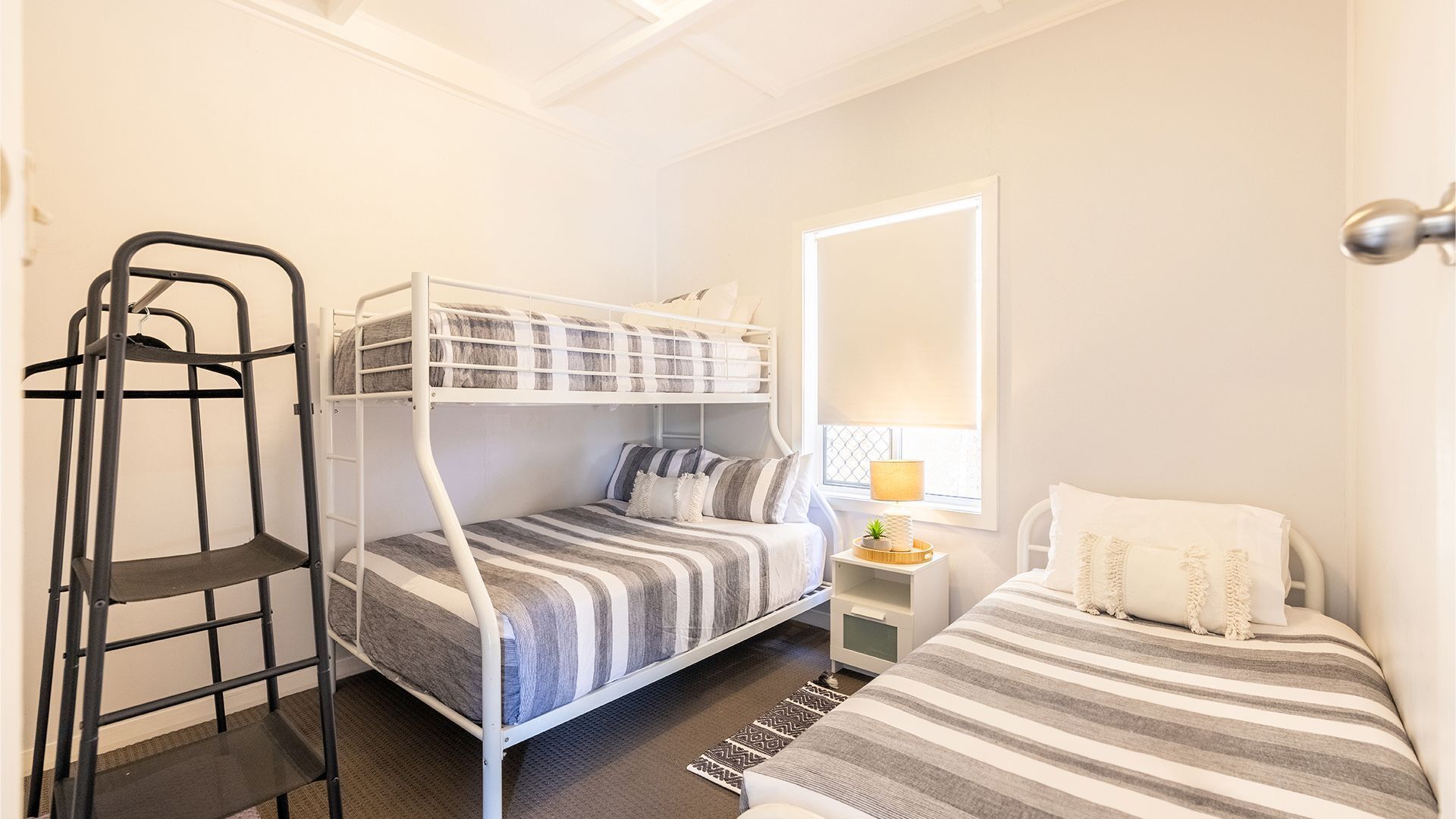 Ein kleines Zimmer mit Etagenbetten, einer Treppe, einem kleinen Nachttisch mit Lampe und einem Fenster mit Jalousien.