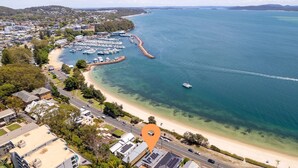 An aerial view of a coastal area with a marina, clear waters, and a sandy beach. - Silver Sands, 29B Victoria Pde - across the road to the water (Nelson Bay)