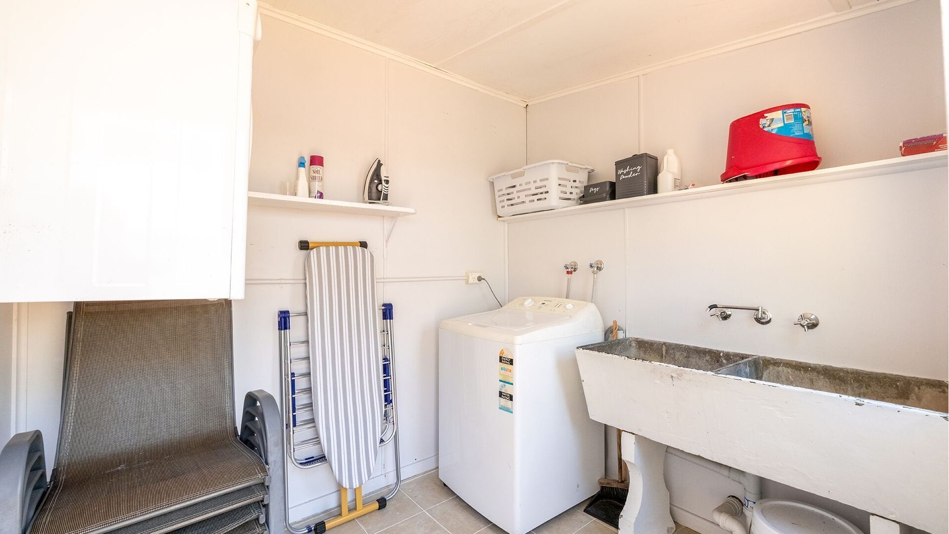 Un baño pequeño y funcional con un lavamanos blanco, un espejo, una cortina de ducha a rayas y un estante con artículos de aseo.