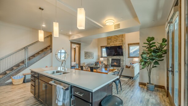 Una cocina amplia con una isla grande, un comedor con chimenea y una escalera que sube a un nivel superior.