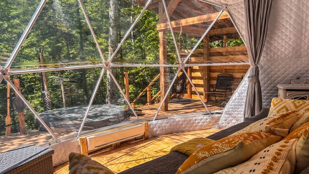 Ein gemütliches Blockhaus mit Glasdecke, Holzvertäfelung und einer bequemen Sitzecke mit Kissen.