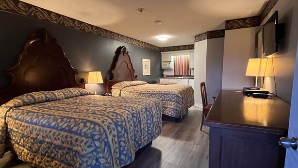 Habitación de hotel con dos camas, un escritorio, una silla, un televisor y un kitchenette.