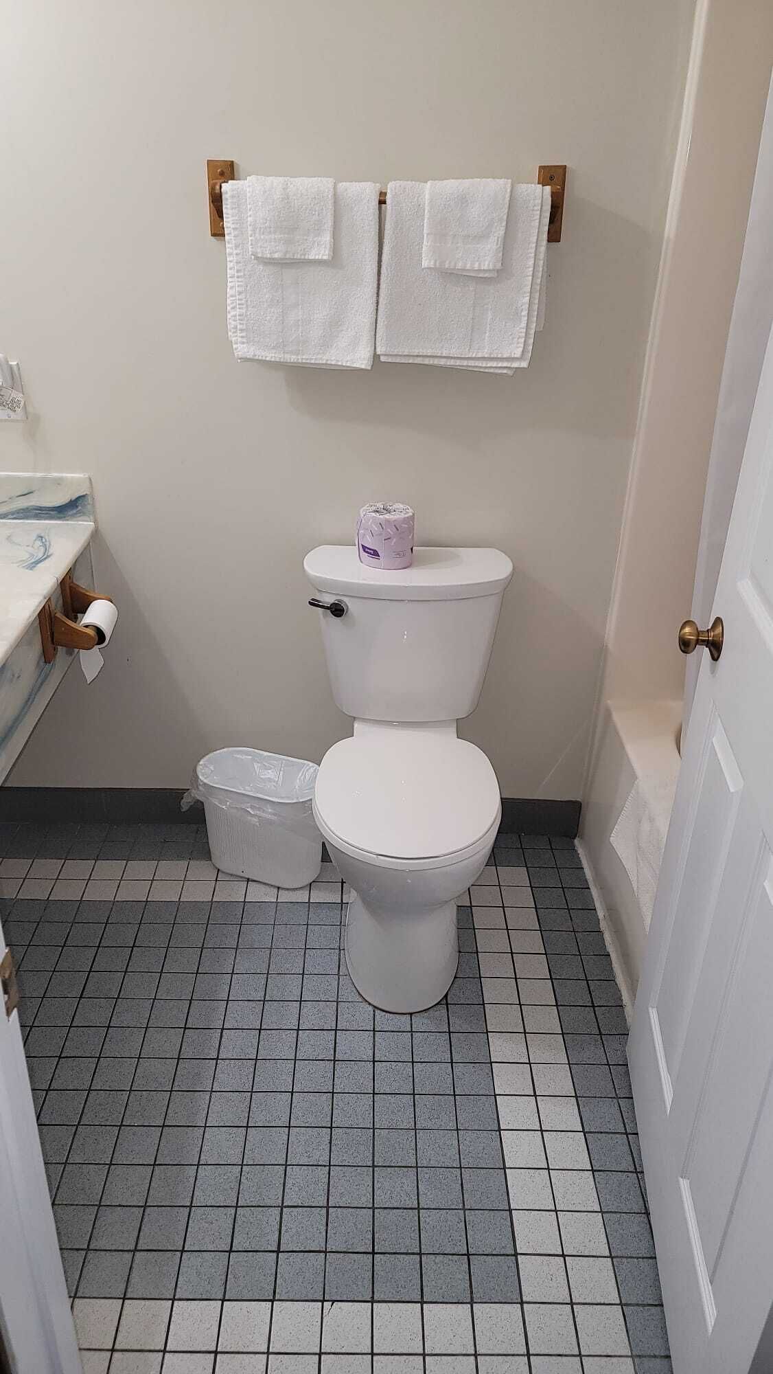 Ein kleines, sauberes Badezimmer mit Toilette, zwei weiße Handtücher an einem Handtuchhalter, einer Toilettenpapierrolle und einem Papierkorb.