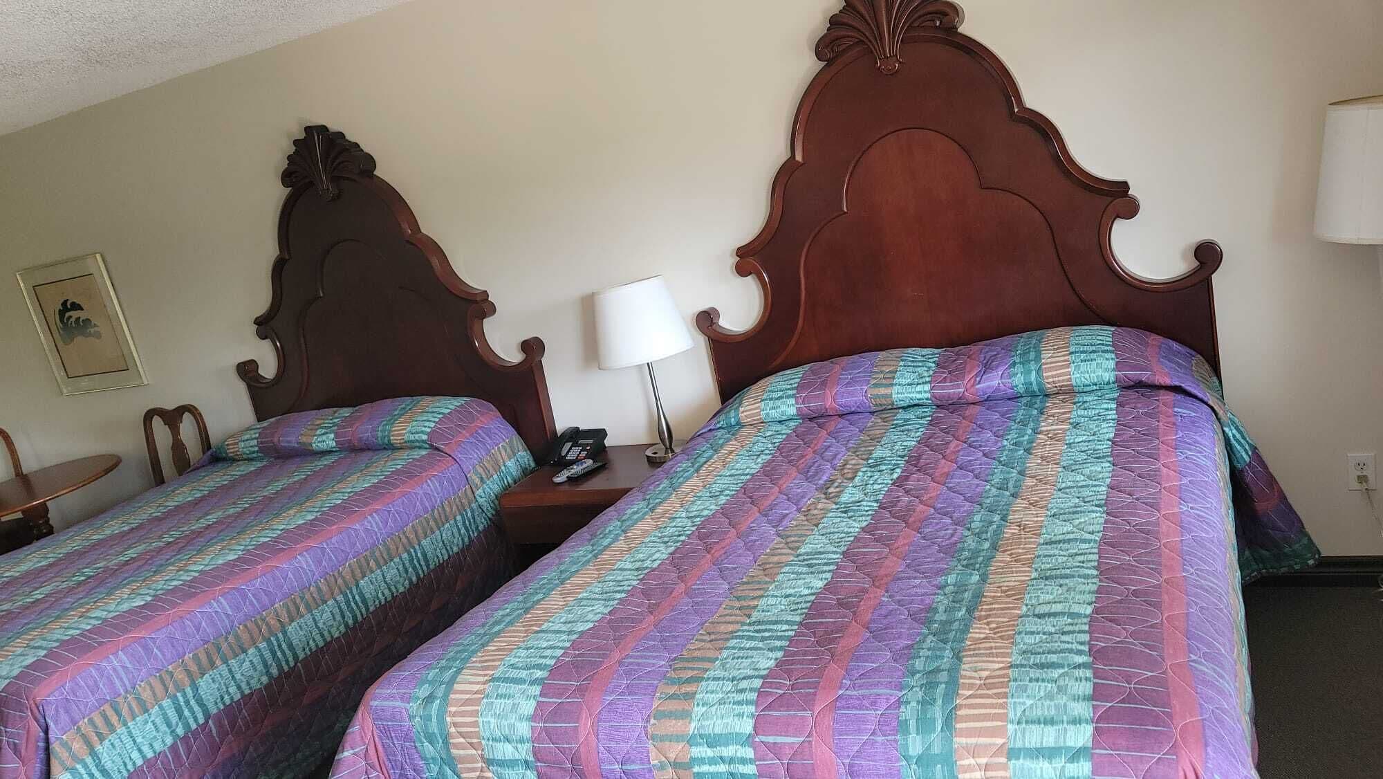 Dos camas de madera con cabeceros a juego, una mesita de noche con lámpara y un cuadro en la pared.