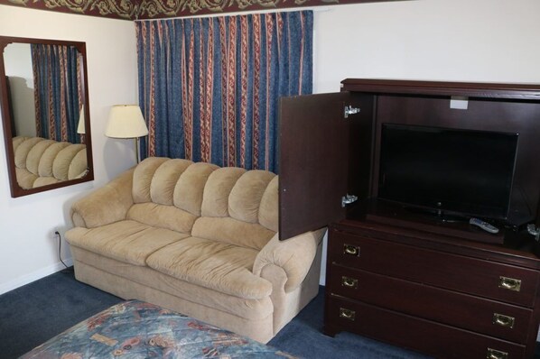 Una habitación con un sofá beige, un aparador de madera oscura con un televisor de pantalla plana, un tapete estampado y un espejo en la pared.