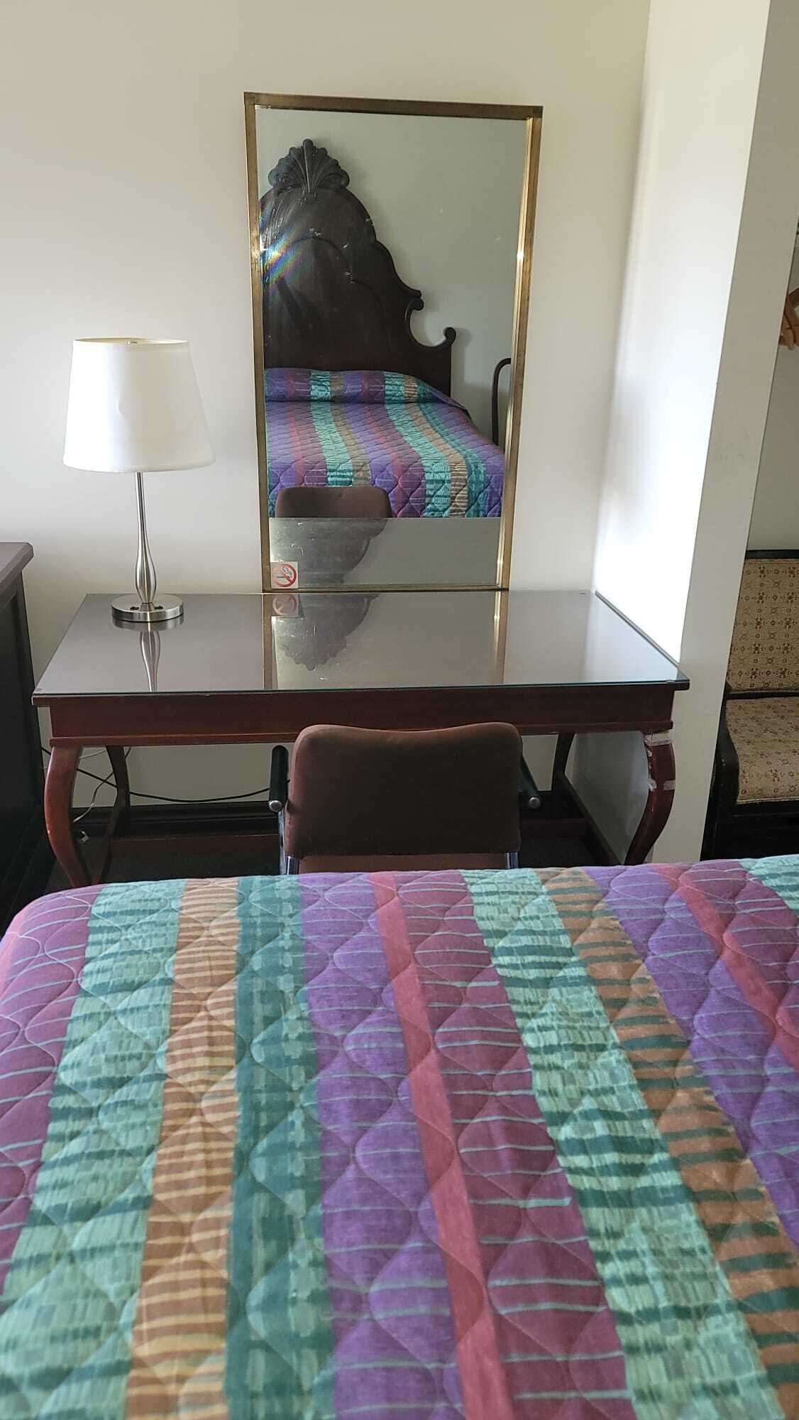 Una habitación de hotel con cama, escritorio, silla y lámpara.