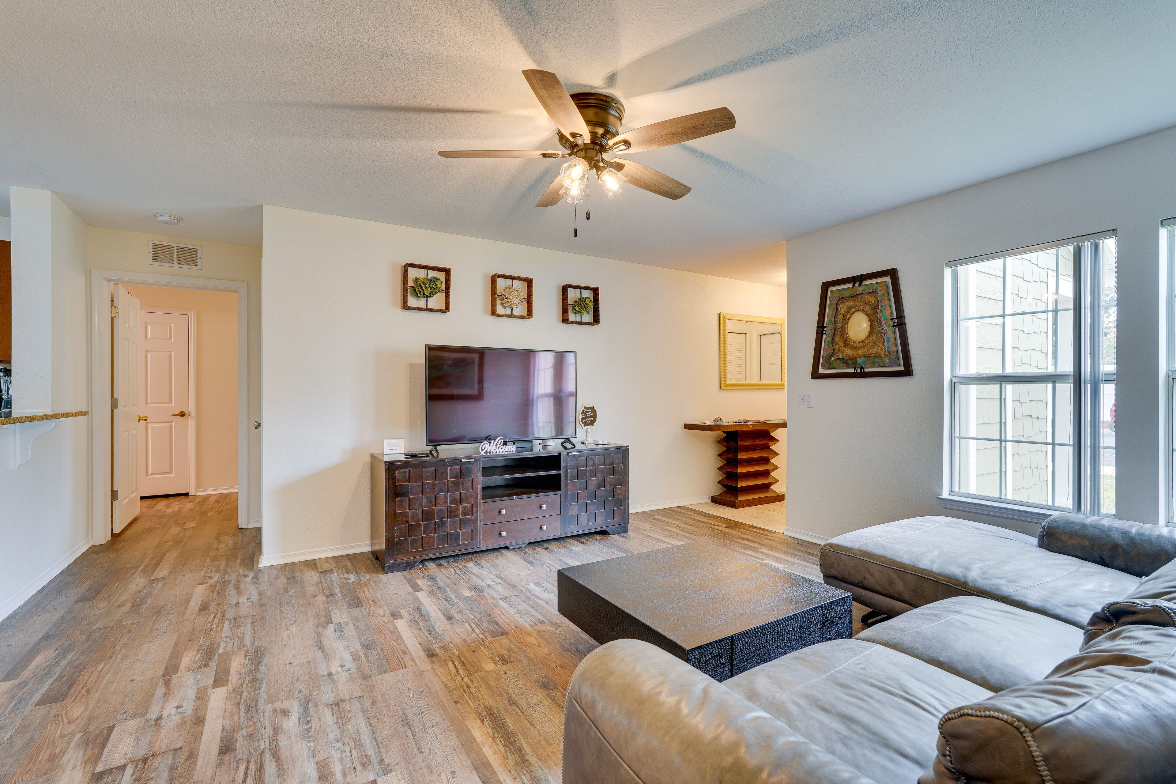 A modern living room with hardwood flooring, a ceiling fan, a flat-screen TV, a leather sofa, and a wooden sideboard.