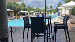 Zona junto a la piscina con sillas de descanso y sombrillas, una terraza de madera y vistas a la piscina.