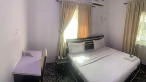 Habitación de hotel con cama, escritorio y silla. Tiene una ventana con cortinas y un equipo de aire acondicionado en la pared.
