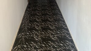 Un pasillo con piso de mármol negro, un extintor rojo sujeto a la pared y una puerta al final.