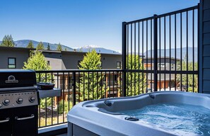 Un balcone con idromassaggio, barbecue e vista su una catena montuosa.