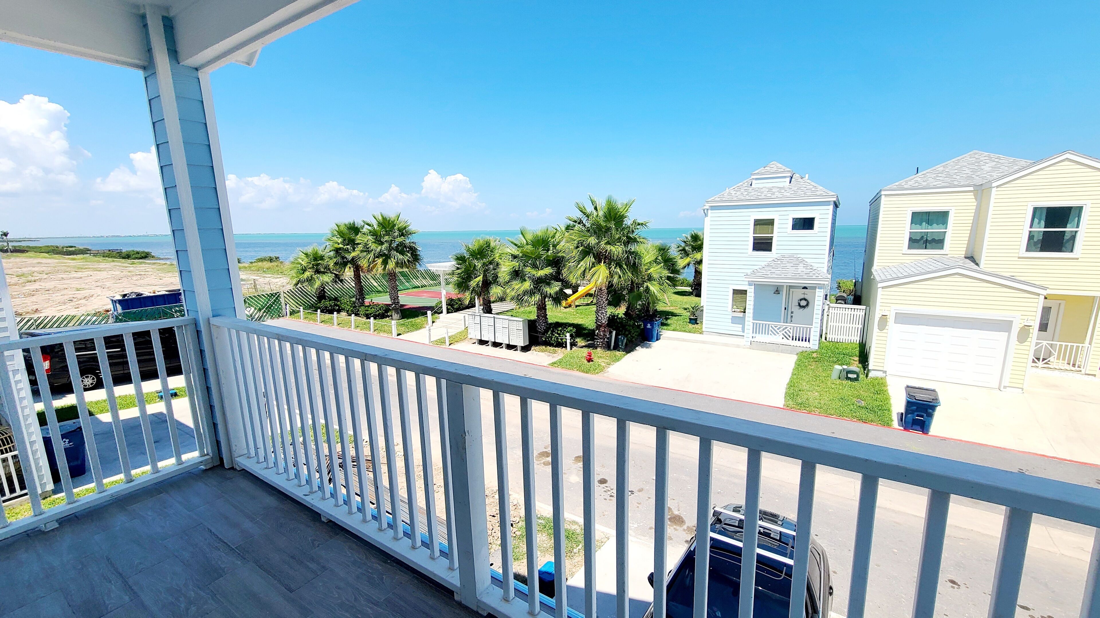 A balcony with a view of a beach, palm trees, and houses.