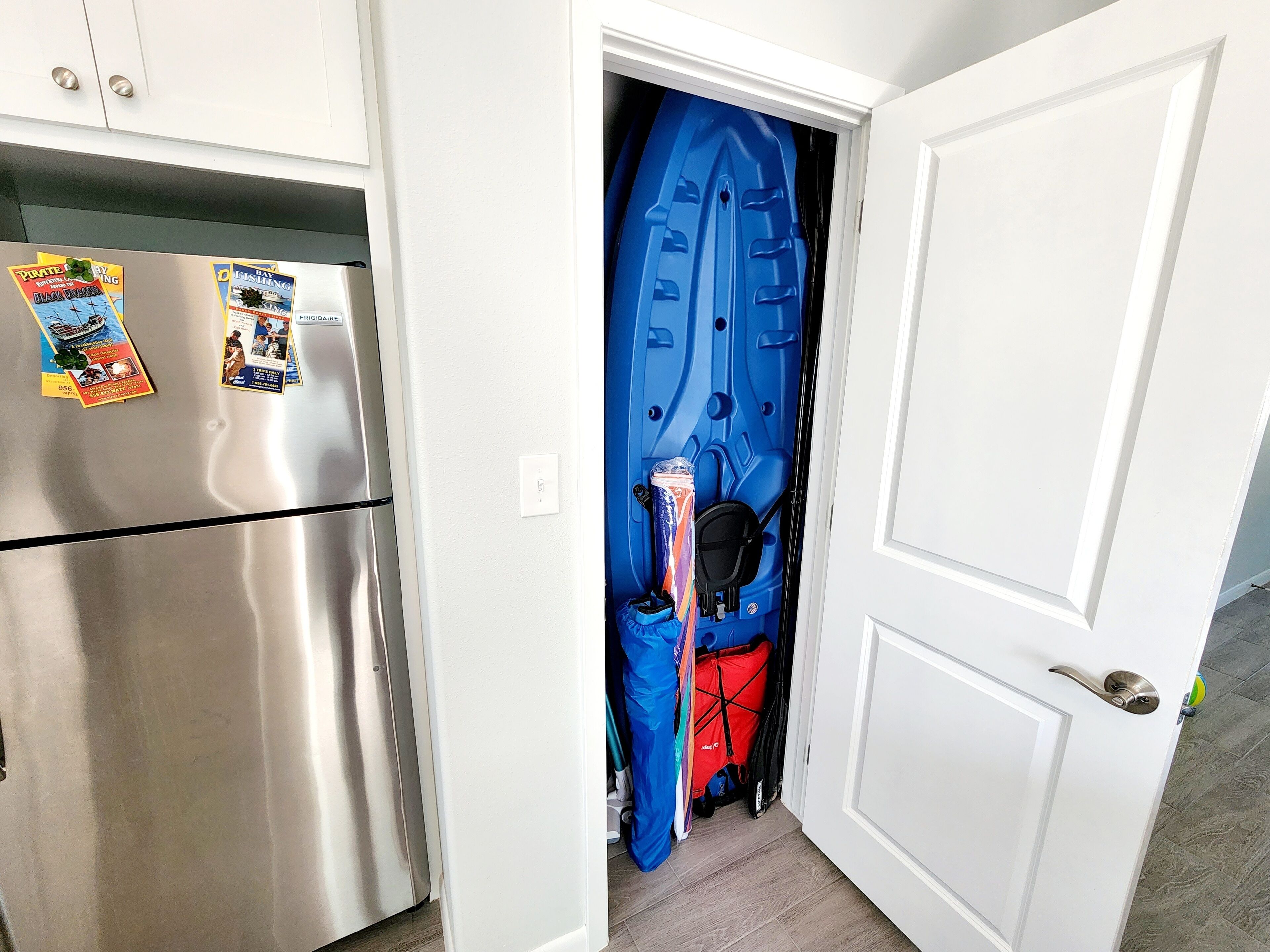 Une cuisine avec un réfrigérateur en acier inoxydable, une porte blanche et une porte bleue donnant sur une pièce avec un mur bleu et un sac rouge.
