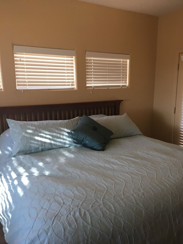 A bedroom with a bed, two windows with blinds, and a door.