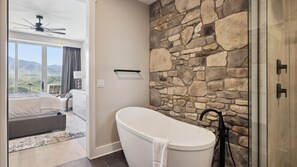 A modern bathroom with a stone wall, a freestanding bathtub, and a shower area. - Jackpot! 3BD Luxe | 3.5 Bath |Sleeps 8 + 1 Free Dollywood, Anakeesta Tkt & More! (Gatlinburg)