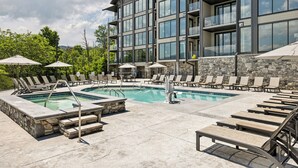 Un edificio moderno con zona de piscina, sillones de baño y sombrillas.