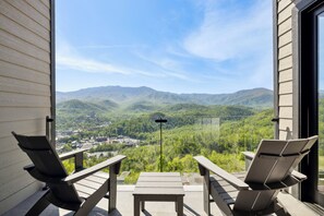 A balcony with two chairs and a table, overlooking a mountainous landscape.