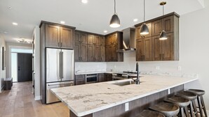 Una cocina moderna con armarios de madera, electrodomésticos de acero inoxidable, encimera de mármol y taburetes de bar.