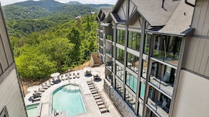 Un hôtel moderne doté d’une piscine, de chaises longues et offrant une vue sur la forêt environnante.