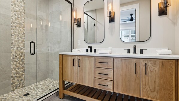 A bathroom with a shower, two sinks, wooden cabinets, and a mirror.