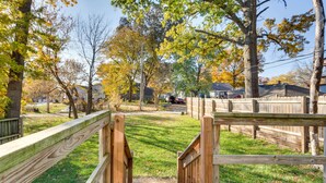 Une porte en bois mène à un espace verdoyant, avec des arbres et des maisons en arrière-plan.
