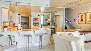 Una cocina moderna con una isla central, taburetes de bar y un comedor con un sofá blanco y una mesa de centro.