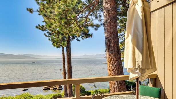 Un balcón con vistas a un lago, una mesa con mantel estampado y un cojín verde.