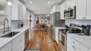 A modern kitchen with white cabinets, stainless steel appliances, and a wooden floor.