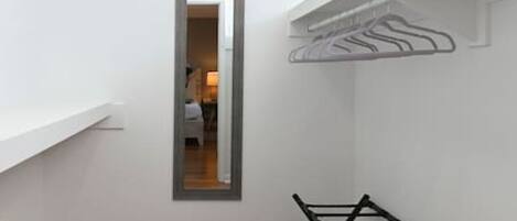 A narrow hallway with wooden flooring, a mirror on the wall, and a black folding chair.
