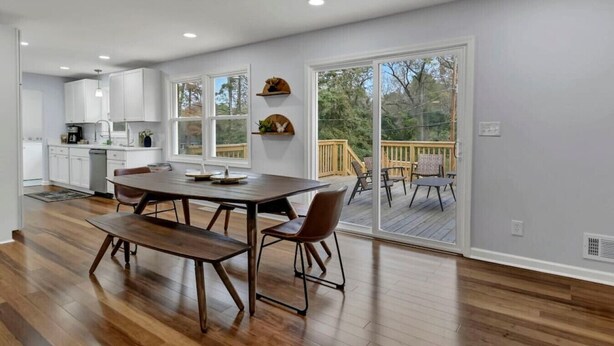 A modern kitchen with white cabinets, a dining area with a wooden table and chairs, and a large sliding glass door leading to an outdoor deck.