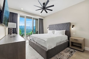 Une chambre avec un lit, un bureau, une télévision, un ventilateur de plafond et une vue par la fenêtre.