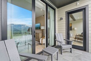Un balcon avec des portes-fenêtres, une vue sur les montagnes et un coin salon avec deux fauteuils.