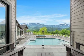 A pool area with lounge chairs, a hot tub, and a mountain view.