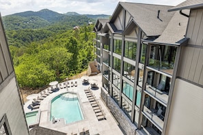 A modern hotel with a rooftop pool, lounge chairs, and a scenic mountain view.
