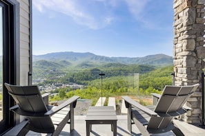A balcony with two chairs and a table, overlooking a mountainous landscape.