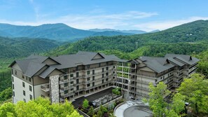 A multi-story hotel with a central courtyard, surrounded by lush greenery and mountains in the background.