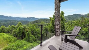 A balcony with a stone pillar, a wooden chair, and a bench overlooking a mountainous landscape. - Stylish Modern 3 BR Condo + Views (Gatlinburg)