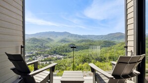 Un balcón con dos sillas y una mesa, con vistas a un paisaje montañoso y un pueblo en la ladera.