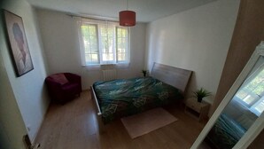 A bedroom with a bed, a chair, a window, and a plant. - Appartement T3, Jardin, Parking (Chaponost)
