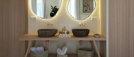 A bathroom with two round mirrors, a wooden vanity, and three wicker baskets under the counter.