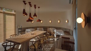 A dining area with a long wooden table, multiple chairs, hanging pendant lights, and wall-mounted lights. - Retiro Costiña Wellness&Villas (Santa Comba)