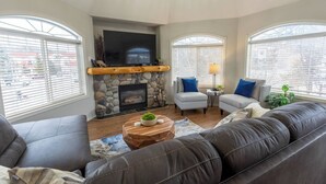 A living room with a stone fireplace, two armchairs, a sofa, and a television. - Riverside Chalet + Suite. Enormous Space (Fernie)