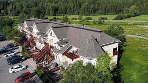 A multi-story building with a sloped roof, a parking lot, and a backdrop of snow-capped mountains. - Riverside Chalet + Suite. Enormous Space (Fernie)