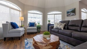 A living room with a grey sofa, a brown leather sofa, and two armchairs. There is a wooden coffee table with a green plant and a blue rug. - Riverside Chalet + Suite. Enormous Space (Fernie)