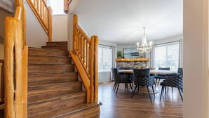 A wooden staircase leading to a dining area with a chandelier, stone wall, and modern chairs. - Riverside Chalet + Suite. Enormous Space (Fernie)