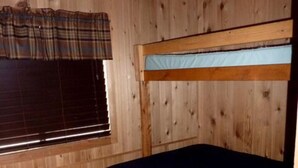 Habitación con literas de madera, una ventana y cortina a cuadros.
